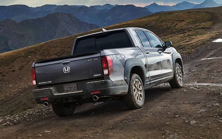 Rear passenger-side view of the 2023 Honda Ridgeline RTL-E in Modern Steel Metallic with available HPD™ Bronze Package driving on a dirt road.