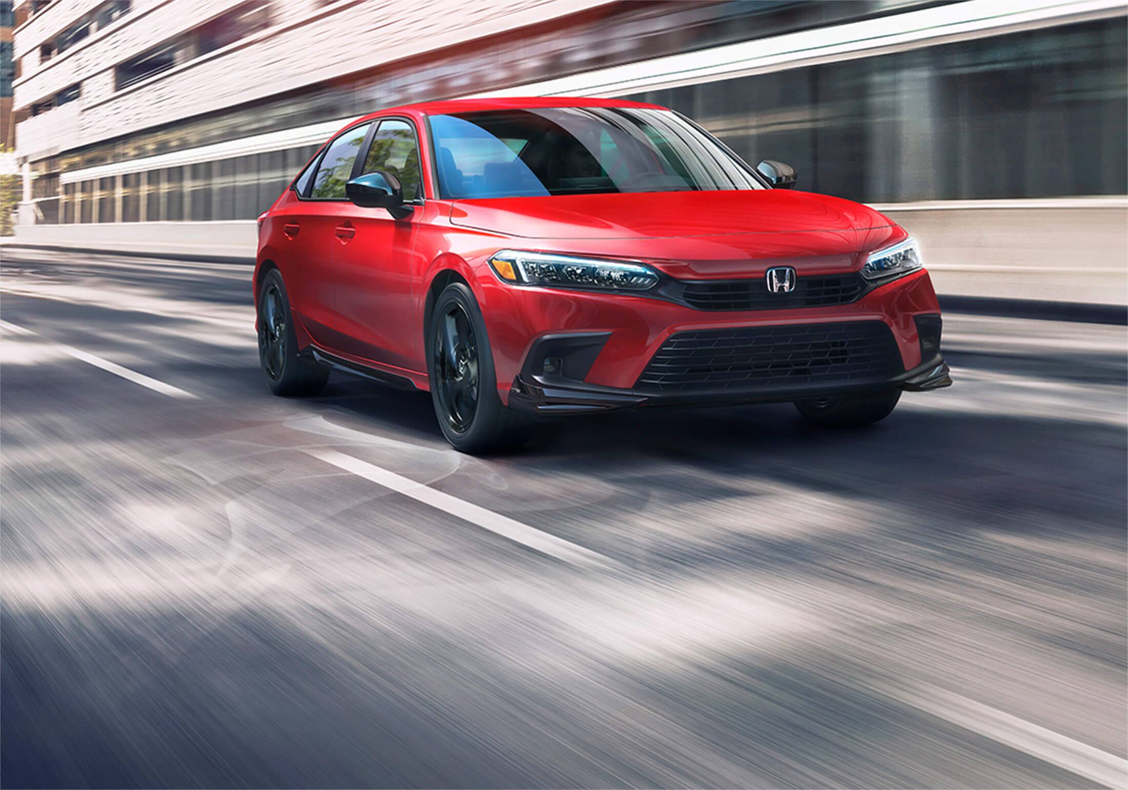 Front passenger-side view of the 2023 Honda Civic Sport Sedan shown with Honda Genuine Accessories in Rallye Red, driving on a city street. 