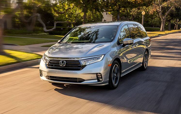 Front driver-side view of the 2023 Honda Odyssey Elite in Lunar Silver Metallic driving on a residential street. 